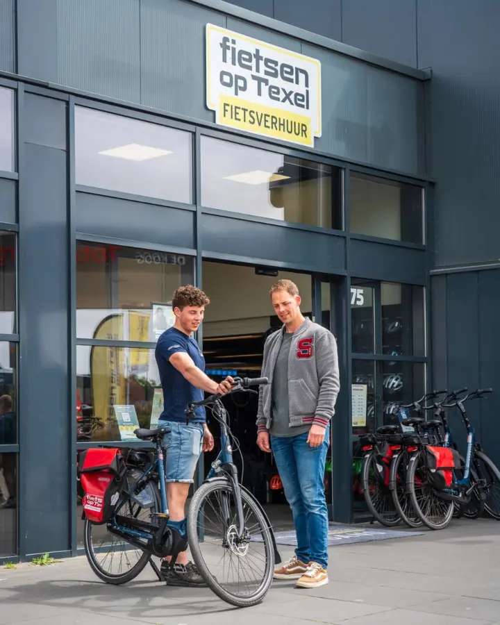 Medewerker van Fietsen op Texel overhandigt een fiets aan een klant bij het depot in De Koog
